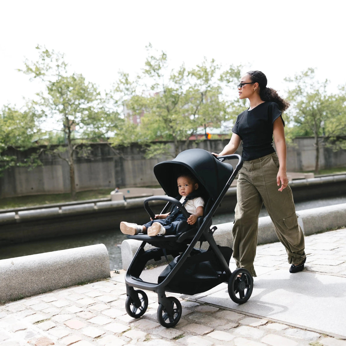 Mum walking with her baby in the UPPAbaby Kona pram in James black
