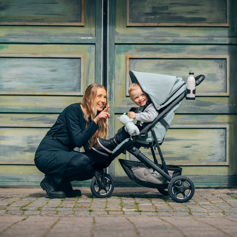 Mother crouching beside a toddler in a Thule Spring 2 stroller on a cobblestone street