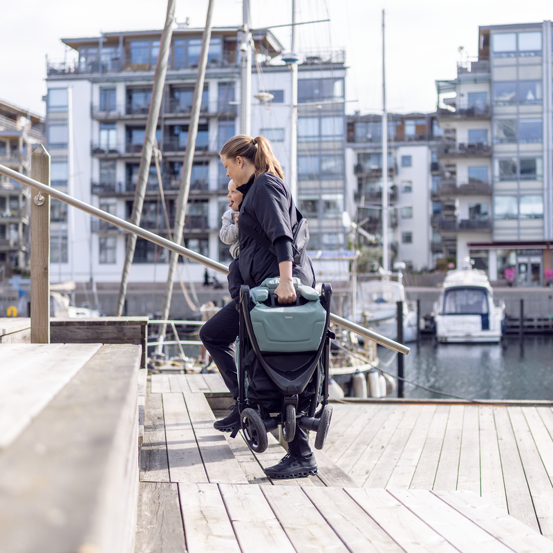 Woman carrying the folded Thule Spring 2 compact stroller by a harbour