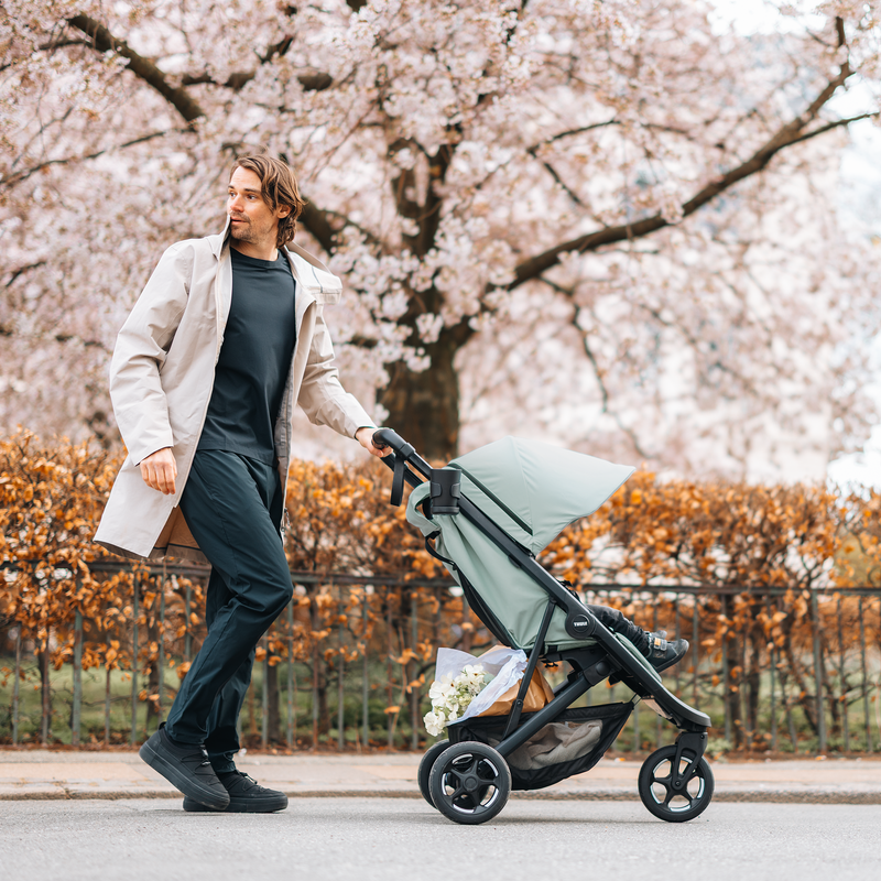 Woman walking with the Thule Spring 2 stroller under cherry blossoms