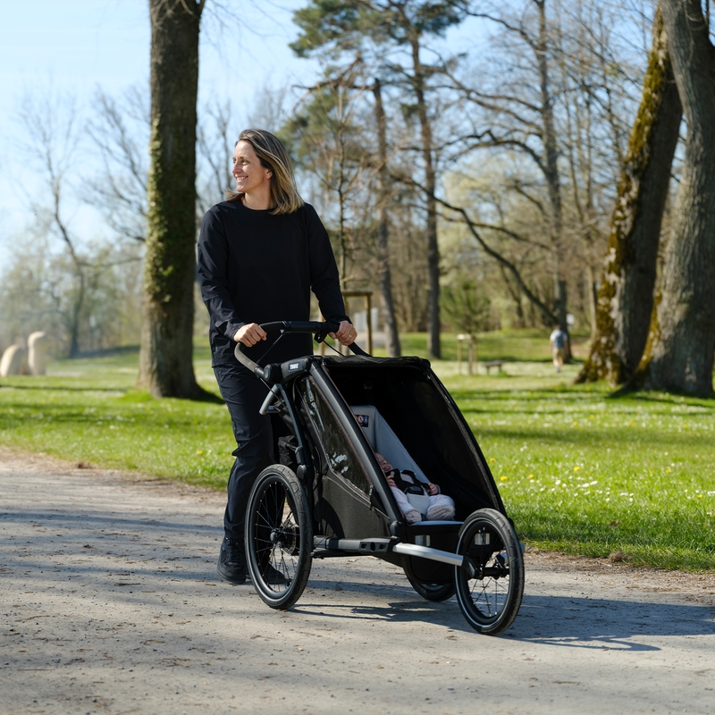 Parent strolling in the park with a Thule Chariot fitted with the infant sling