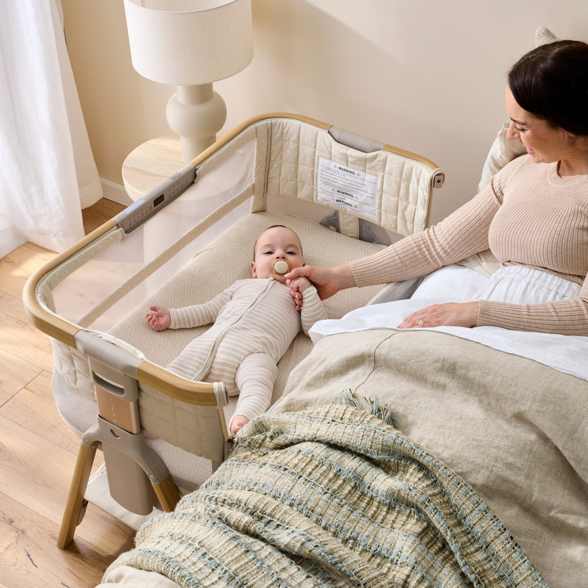 Mum beside her baby sleeping on their back in the CoZee Breeze Sense bedside bassinet