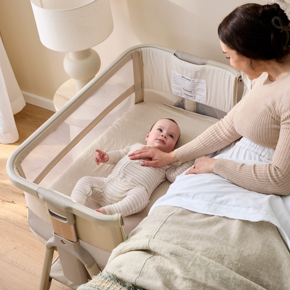 Mum beside her baby sleeping on their back in the CoZee Breeze Zen bedside bassinet