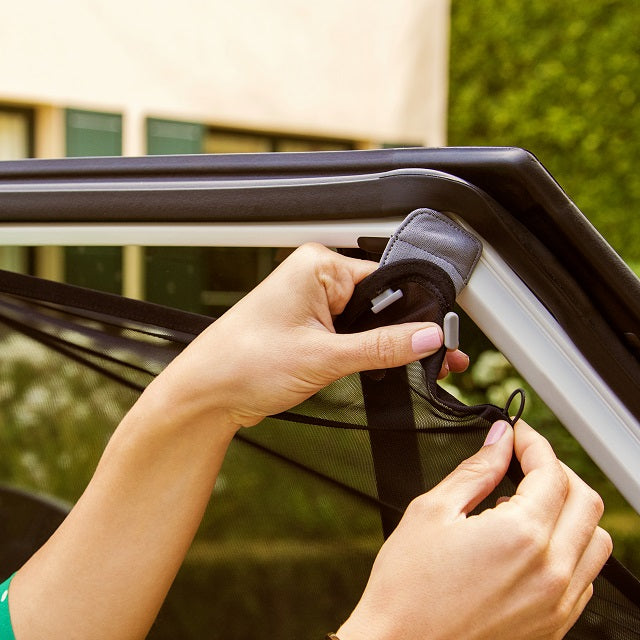 Close-up of hands attaching the Munchkin sun shade mesh to a metal car door frame with magnets