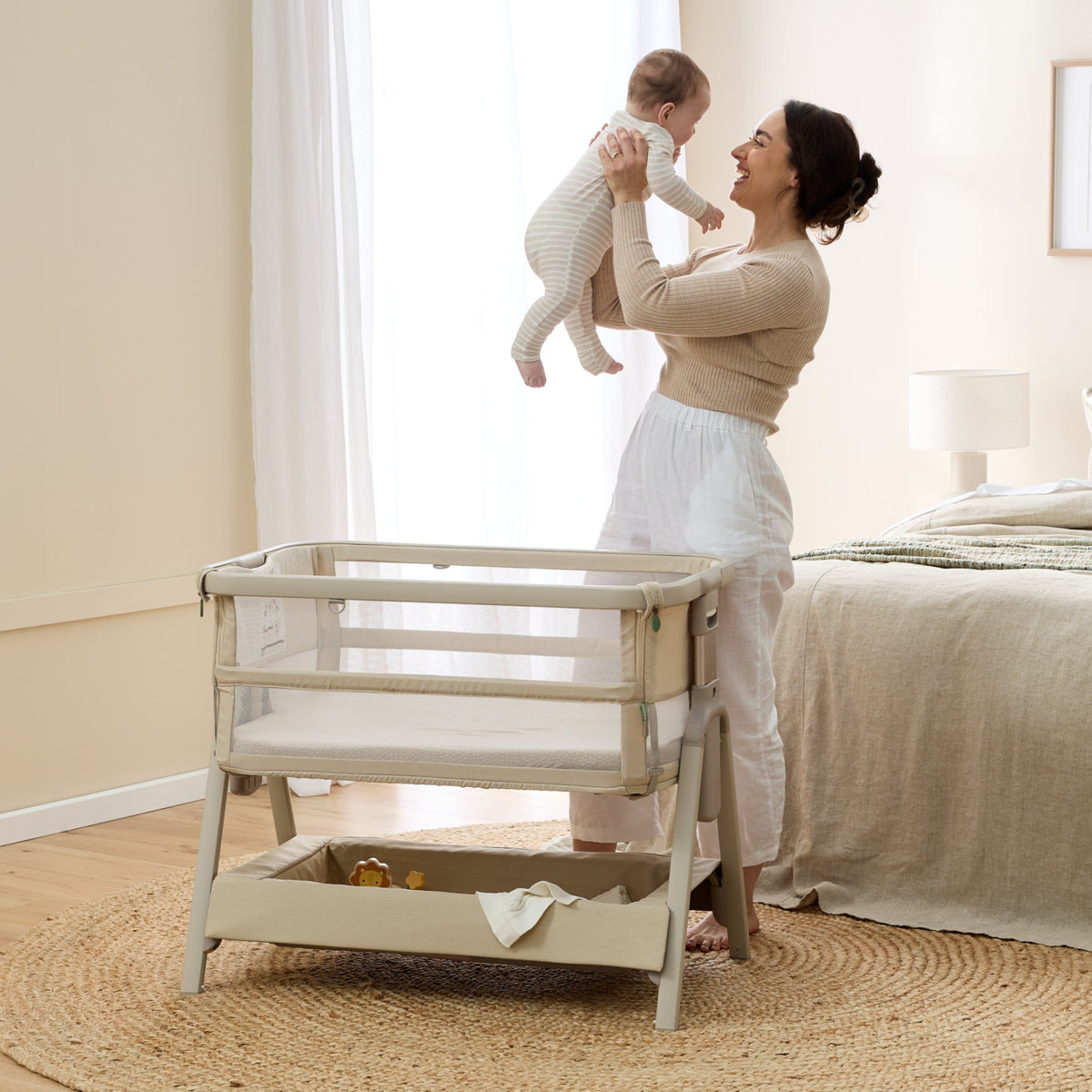 Mum lifting her baby beside the CoZee Breeze Zen bassinet in a bedroom