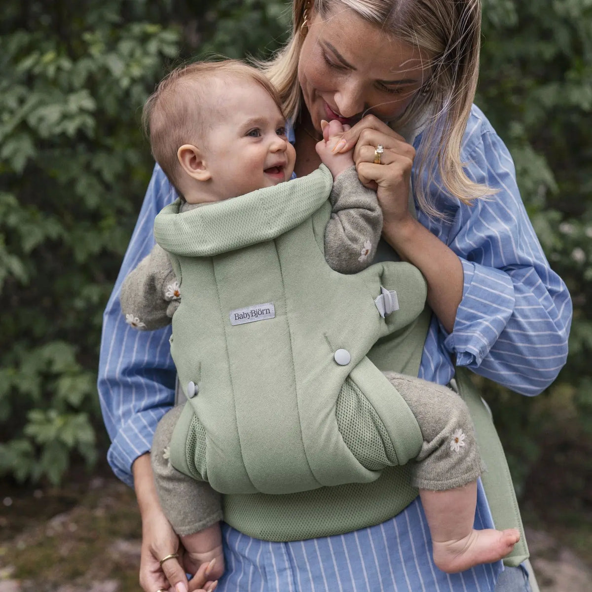 BabyBjorn Baby Carrier Hold Light Green worn outdoors with a smiling baby