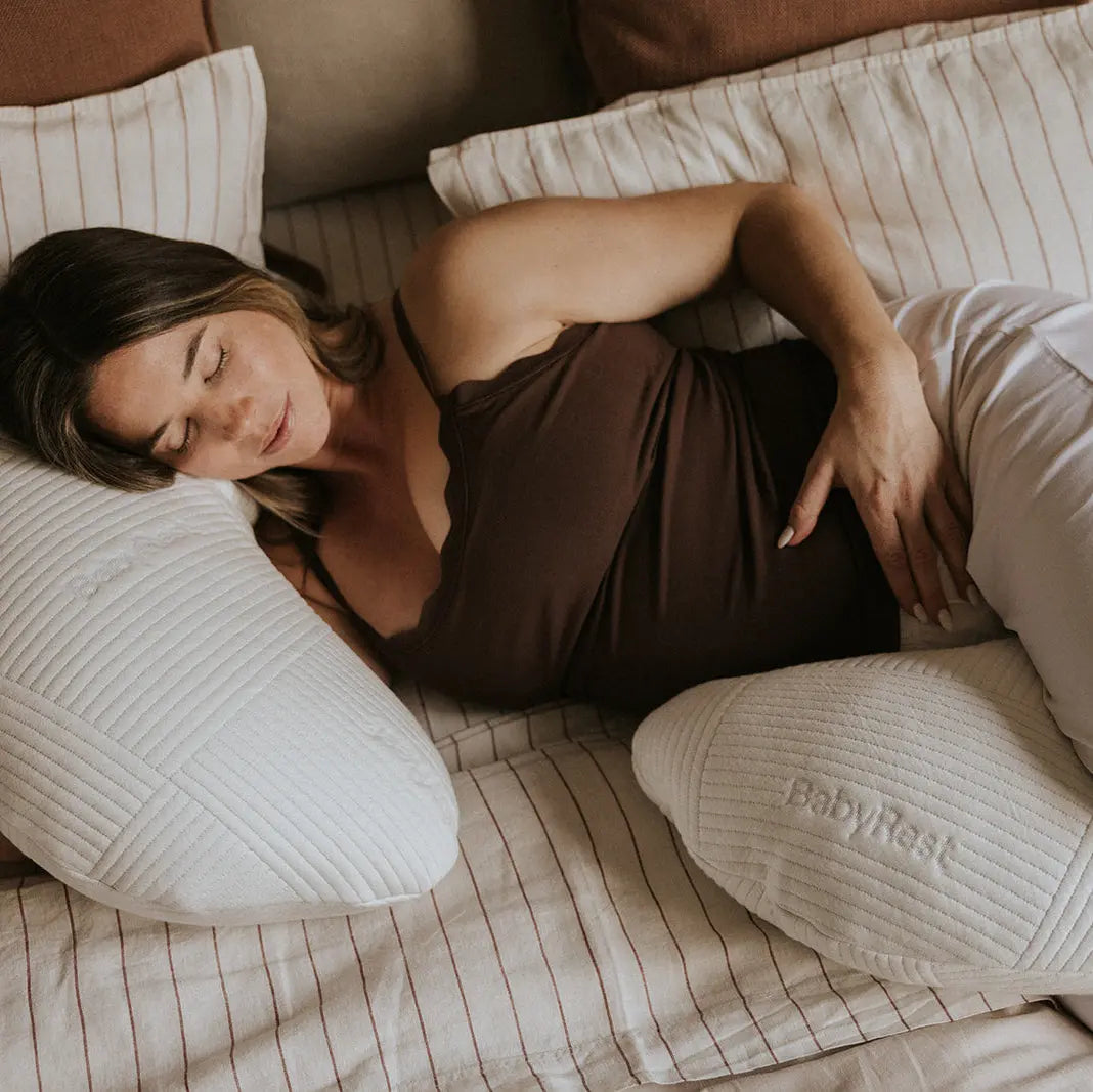 Woman lying on a bed using the Babyrest Haven maternity pillow to support her body during pregnancy