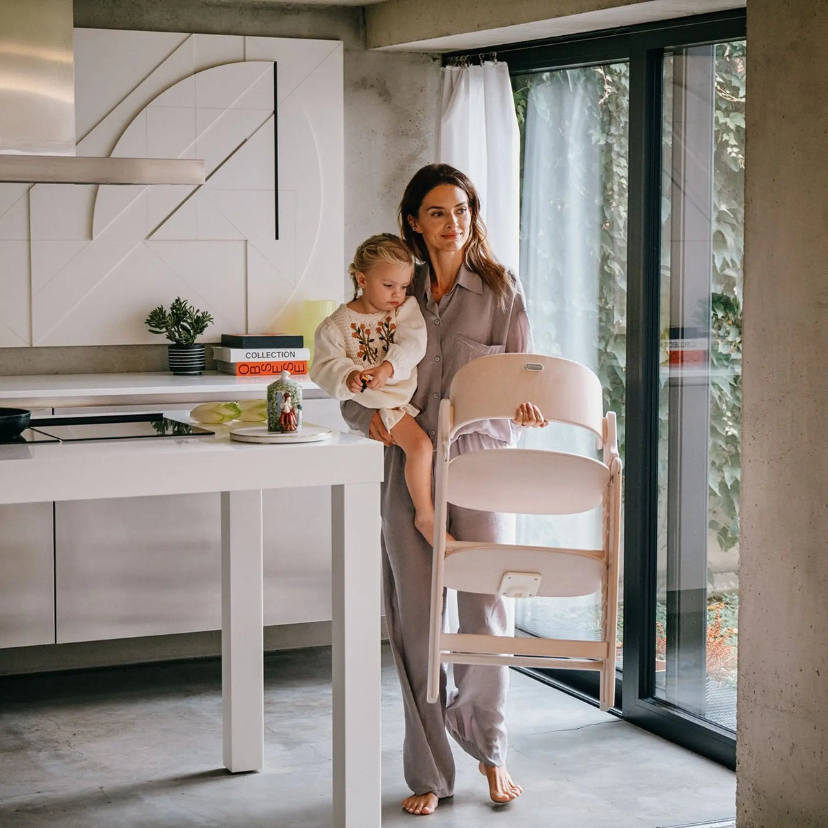 Mum holding her toddler next to the Cybex Click & Fold high chair in the kitchen