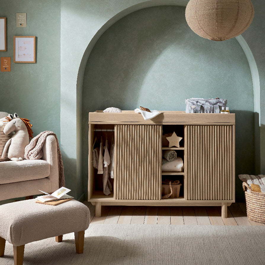 Oska cotbed and wide dresser changer in oak styled together in a nursery