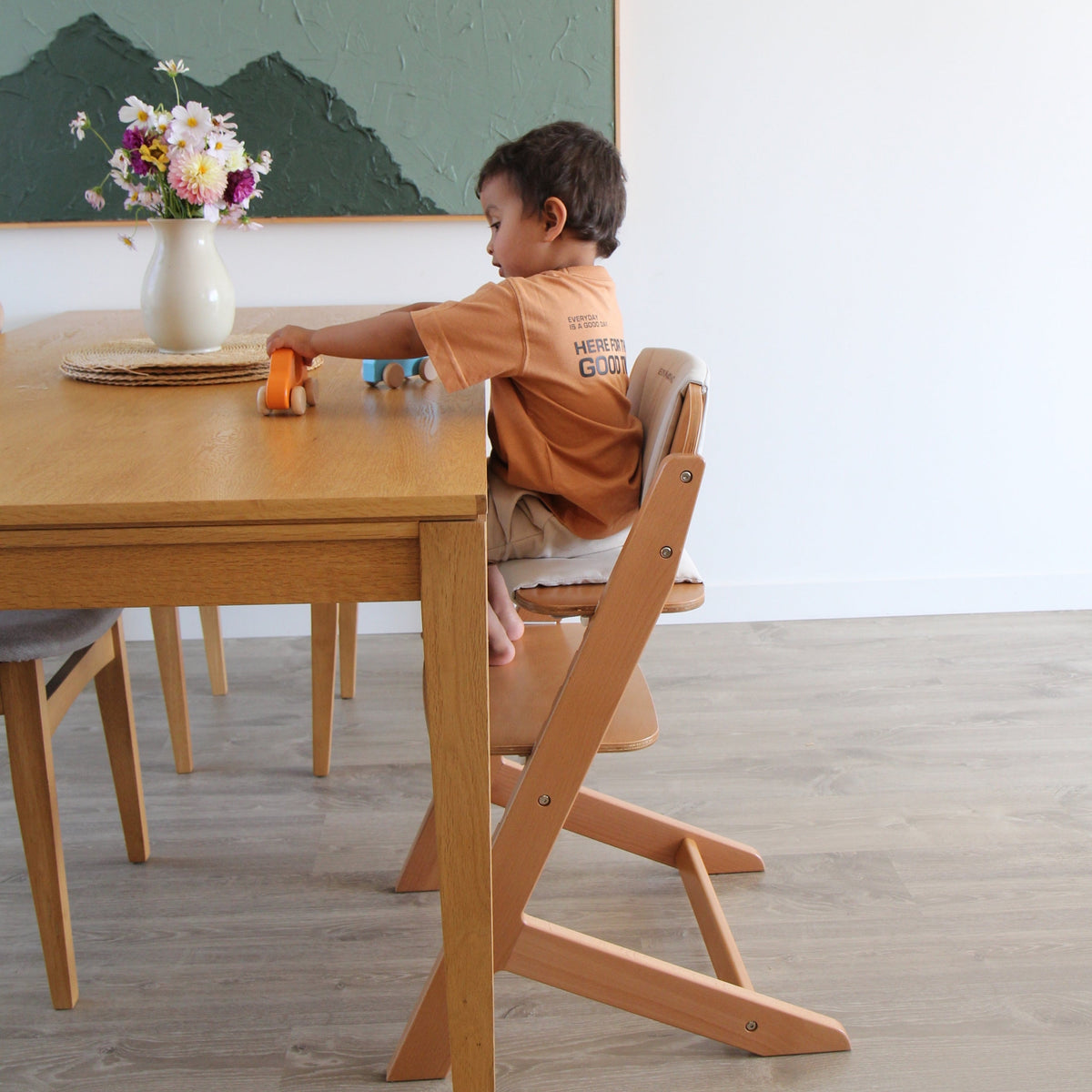 Toddler sitting at the family dining table in the Cariboo Frankie Highchair with the tray removed (shown in Natural)