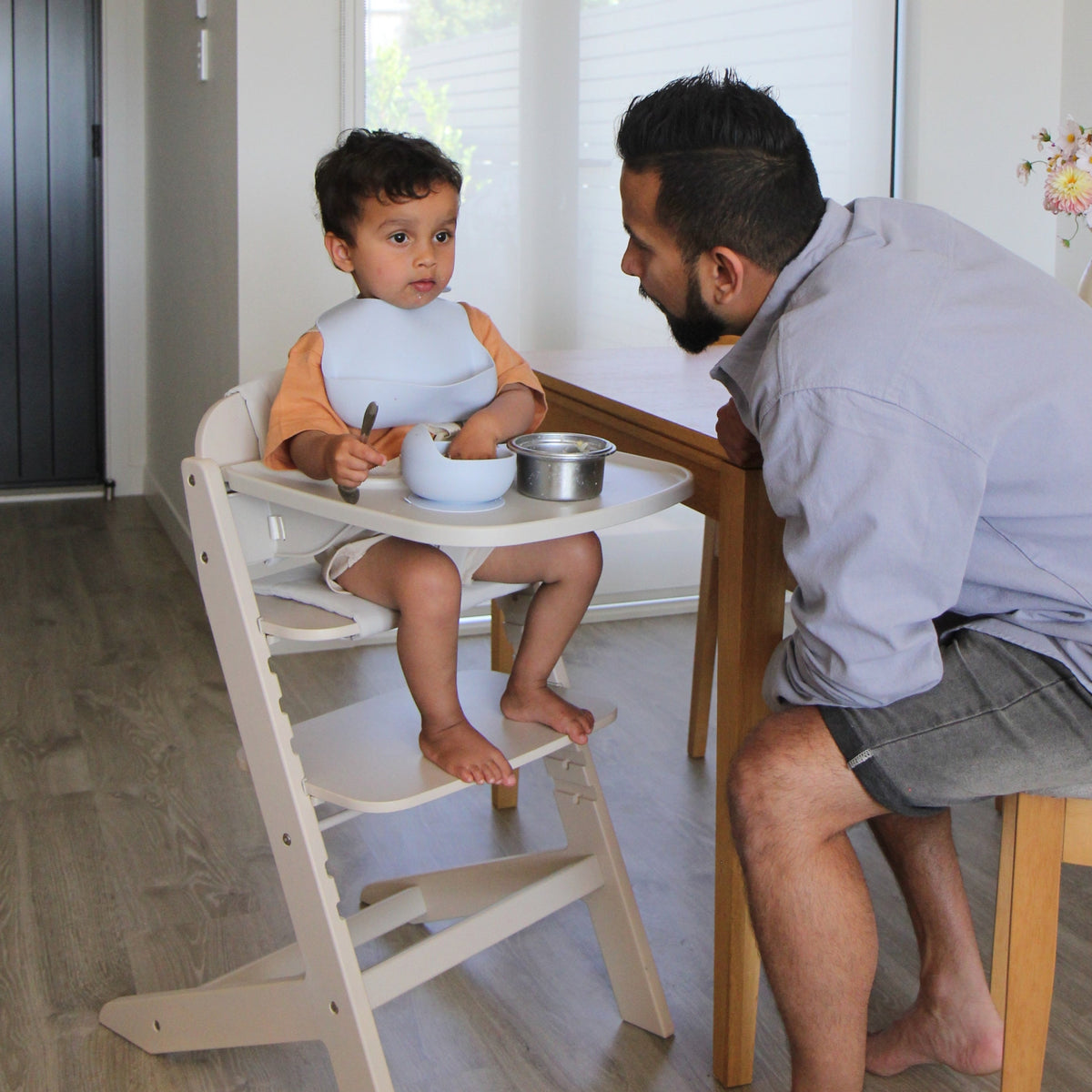 Dad feeding his toddler seated in the Cariboo Frankie Highchair at the dining table, showing the adjustable footrest (shown in Oat)