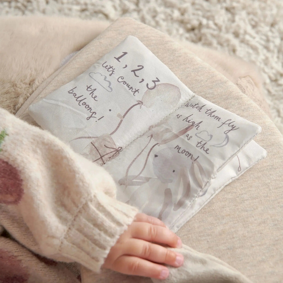 Mamas & Papas Sit & Play floor seat in Welcome to the World Millie & Boris, baby holding the crinkle fabric book