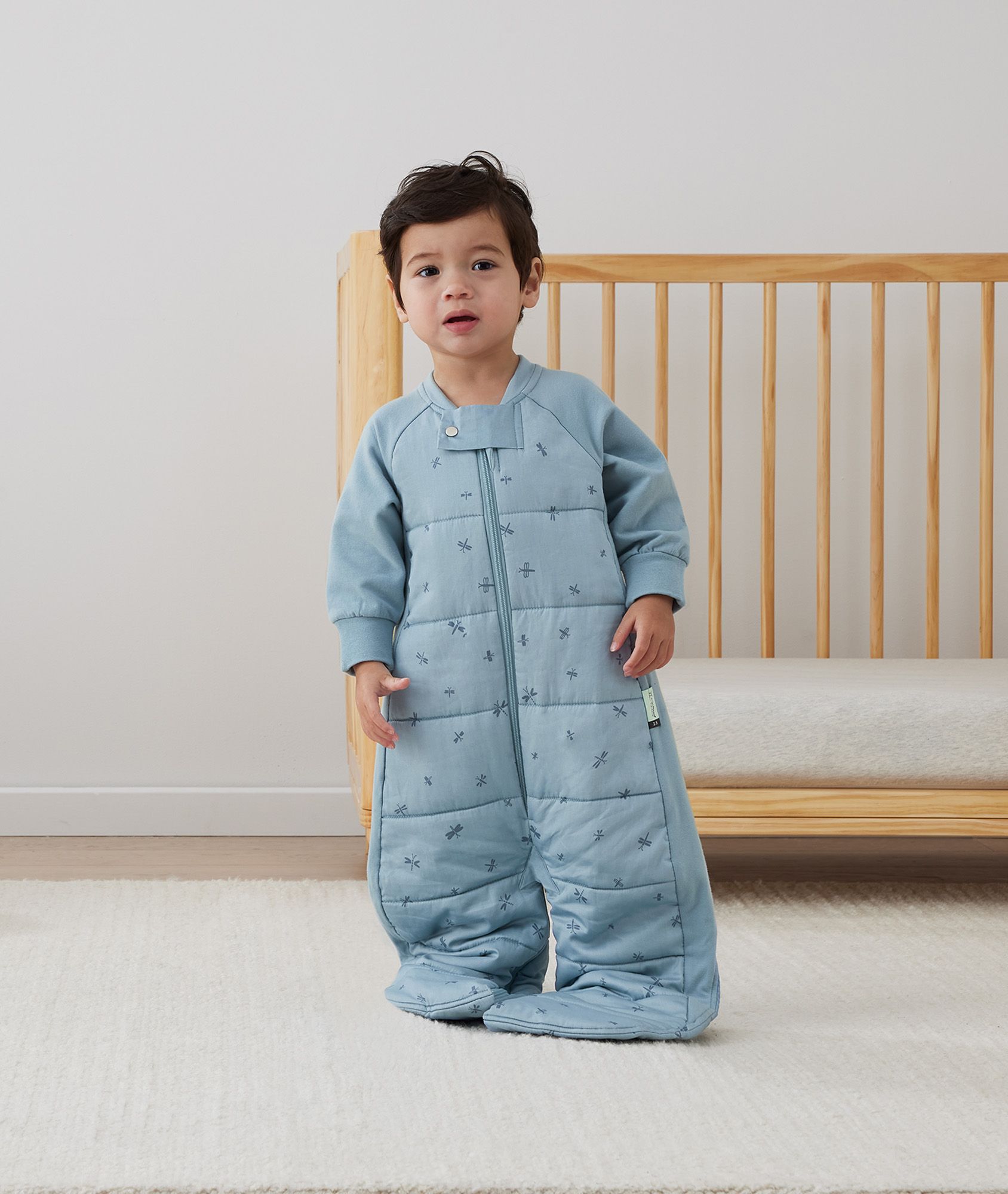 Toddler standing in the ergoPouch Sleep Suit Bag 2.5 TOG Dragonflies with legs unzipped