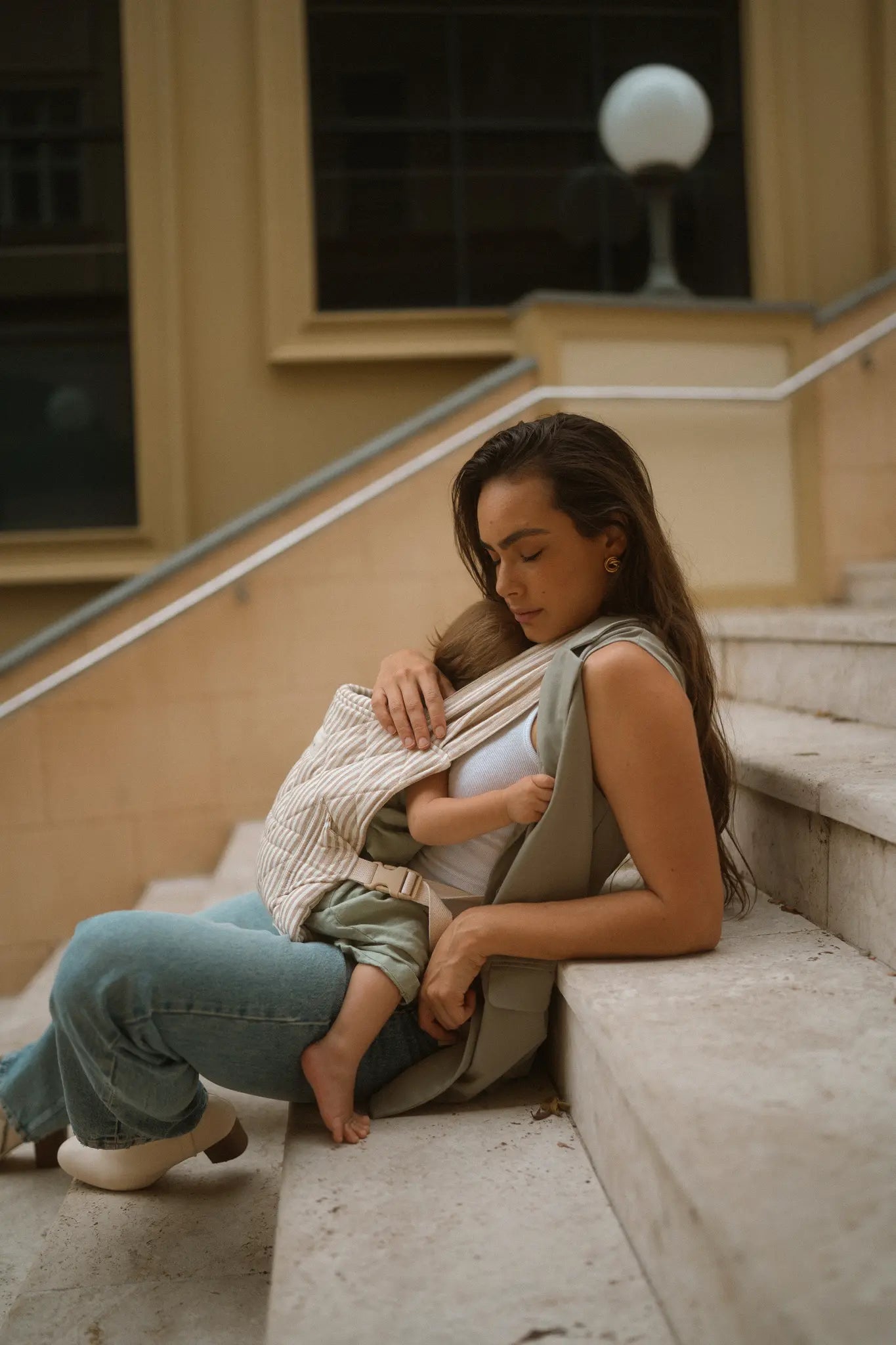 Seated mum rests her cheek on her toddler's head in the Burleigh stripe Daily Carrier