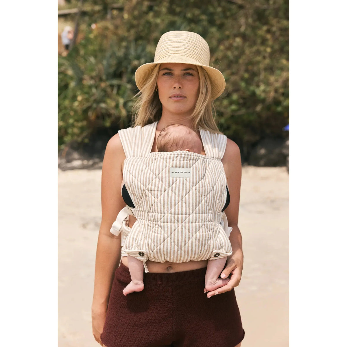 Mum on the sand wearing a sleeping newborn in the Burleigh stripe Daily Carrier