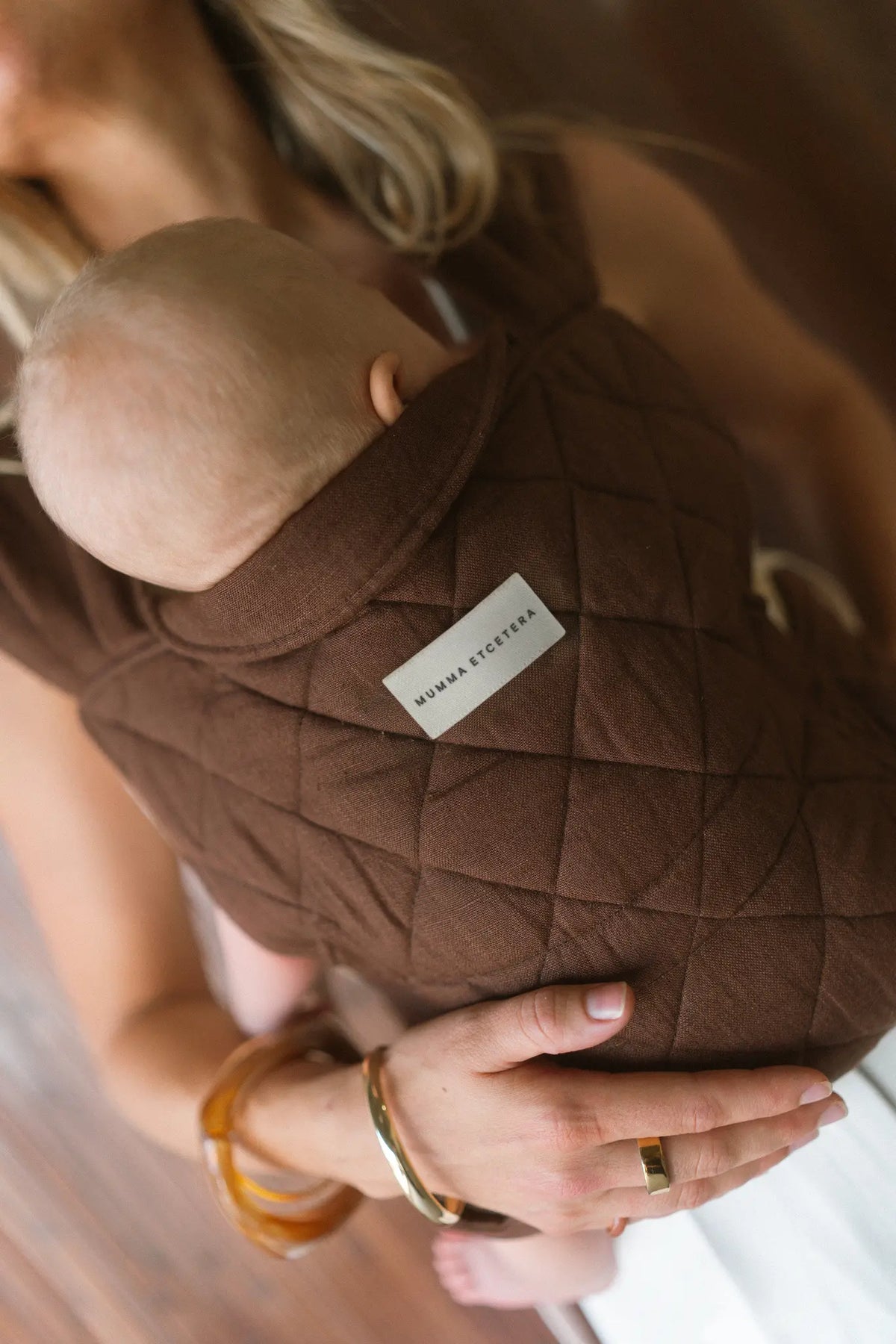 Newborn settled against the quilted Coco linen Daily Carrier, woven brand label in view