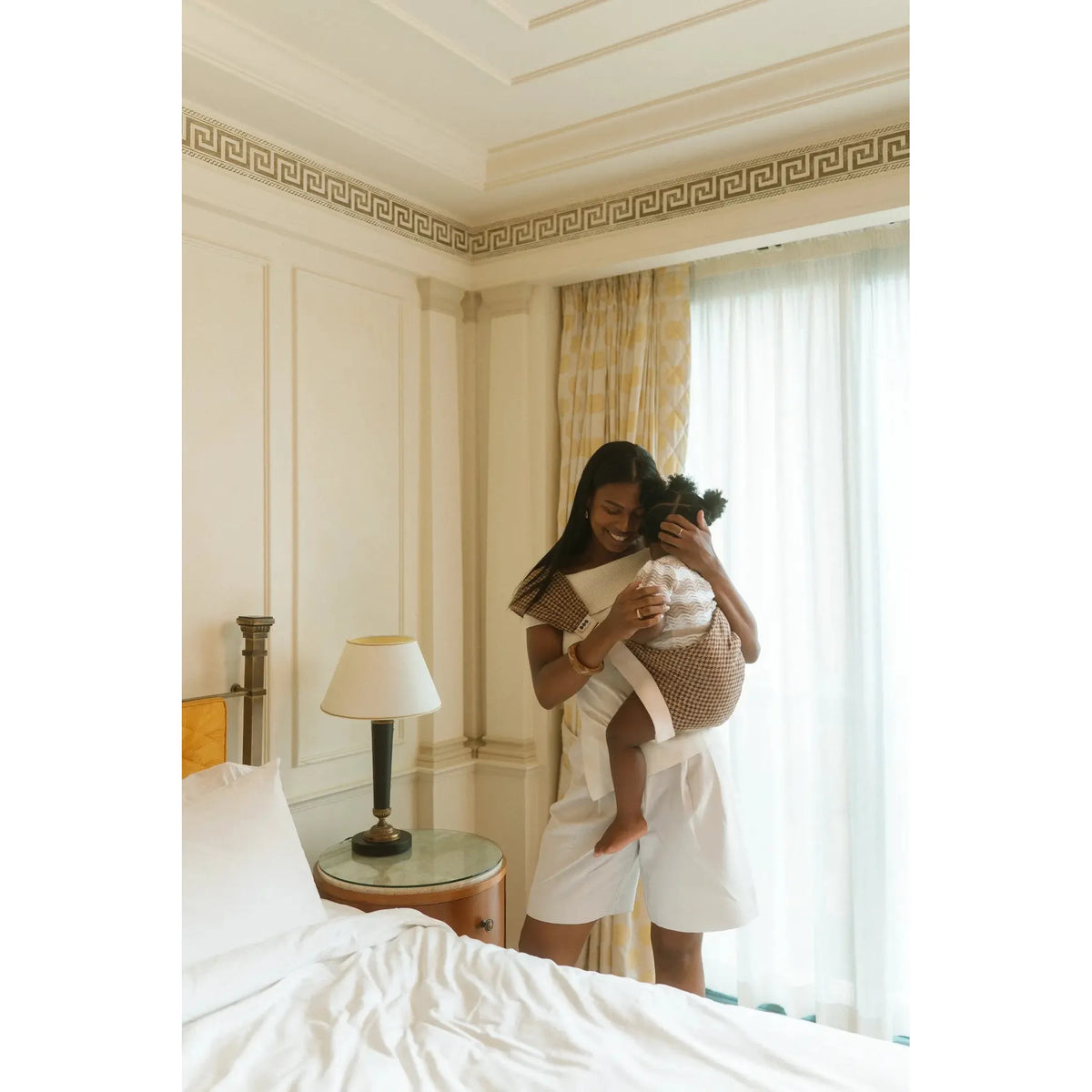 Mum cuddles her toddler close in the Arista houndstooth Hipsy toddler carrier by a sunlit window