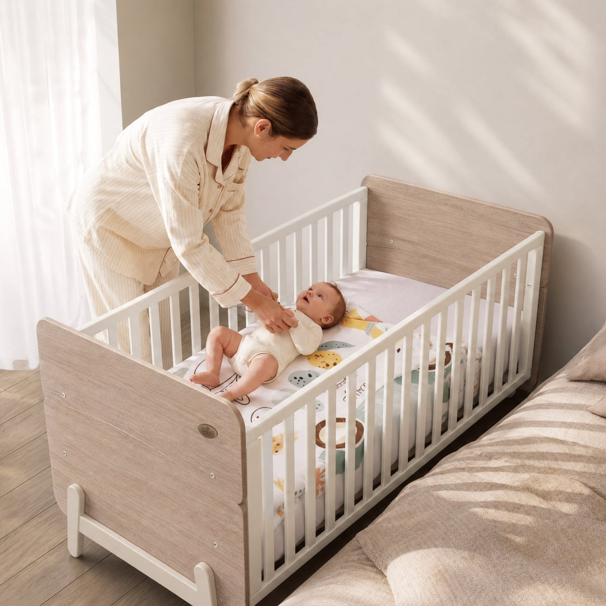 Parent settling baby in the Boori Natty Ergonomic Cot Bed (shown in White & Oak)