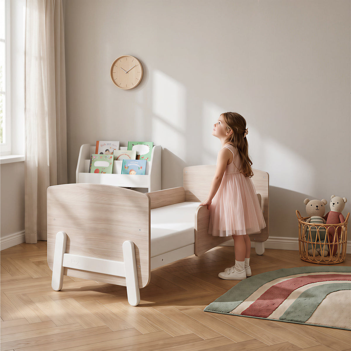 Girl beside the Natty Ergonomic Cot Bed in toddler bed mode (shown in White & Oak)