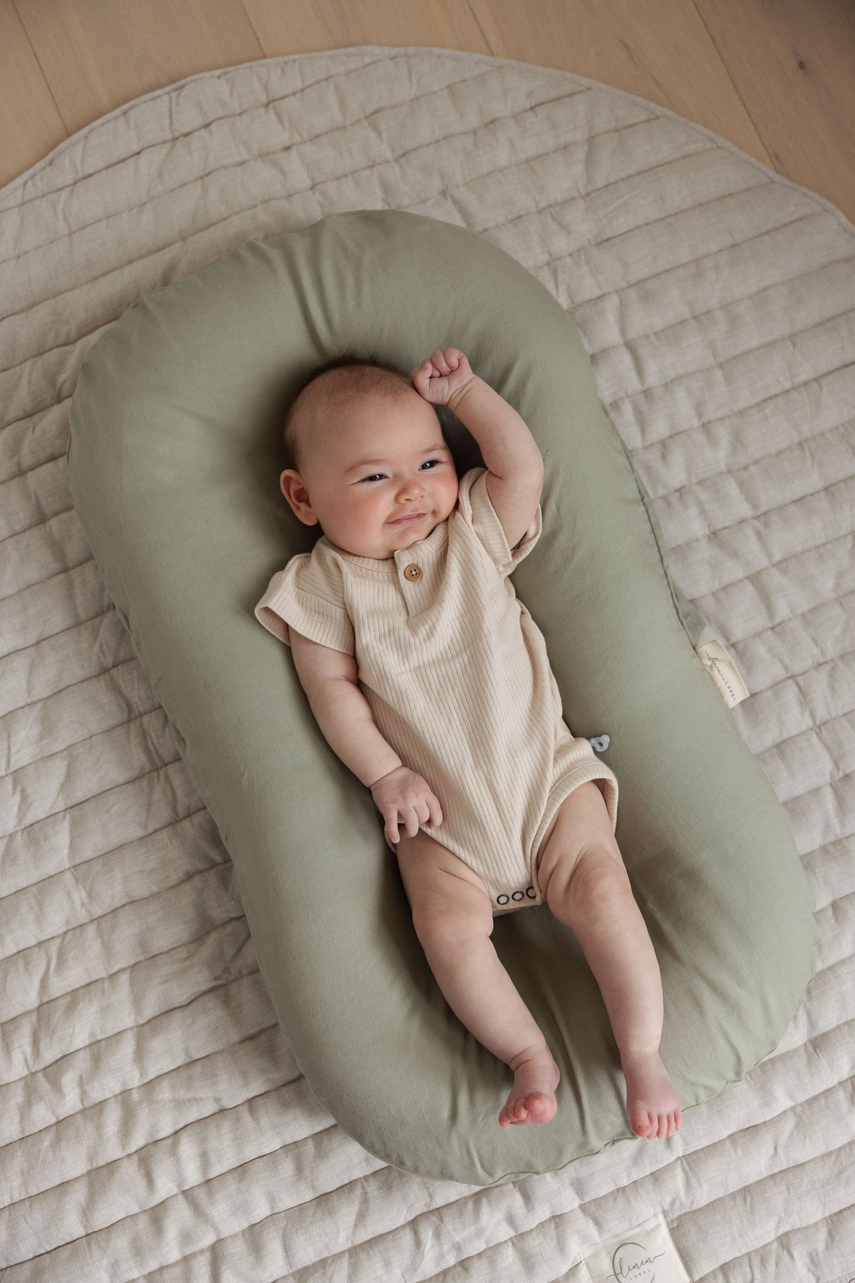 Linen Label baby lounger nest shown on the floor for supervised rest