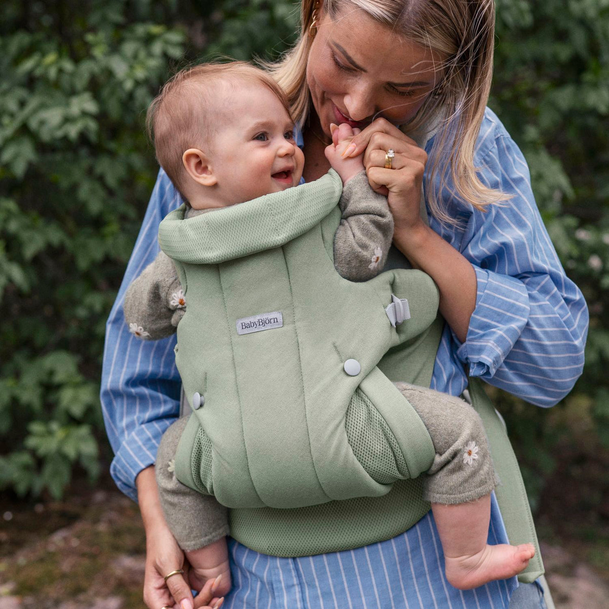 BabyBjorn Baby Carrier Hold Light Green worn outdoors with a smiling baby