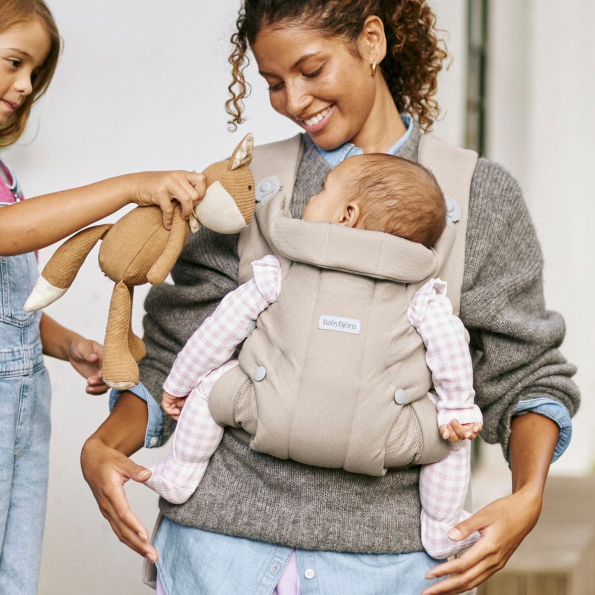 BabyBjorn Baby Carrier Hold Sand Grey worn at home with baby facing in